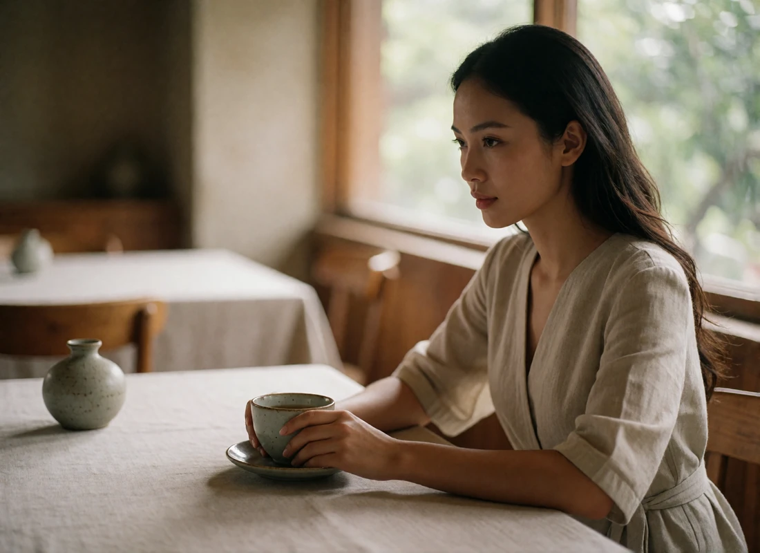 Thai woman seated at a fine-dining restaurant table beside a window, holding a ceramic teacup.
