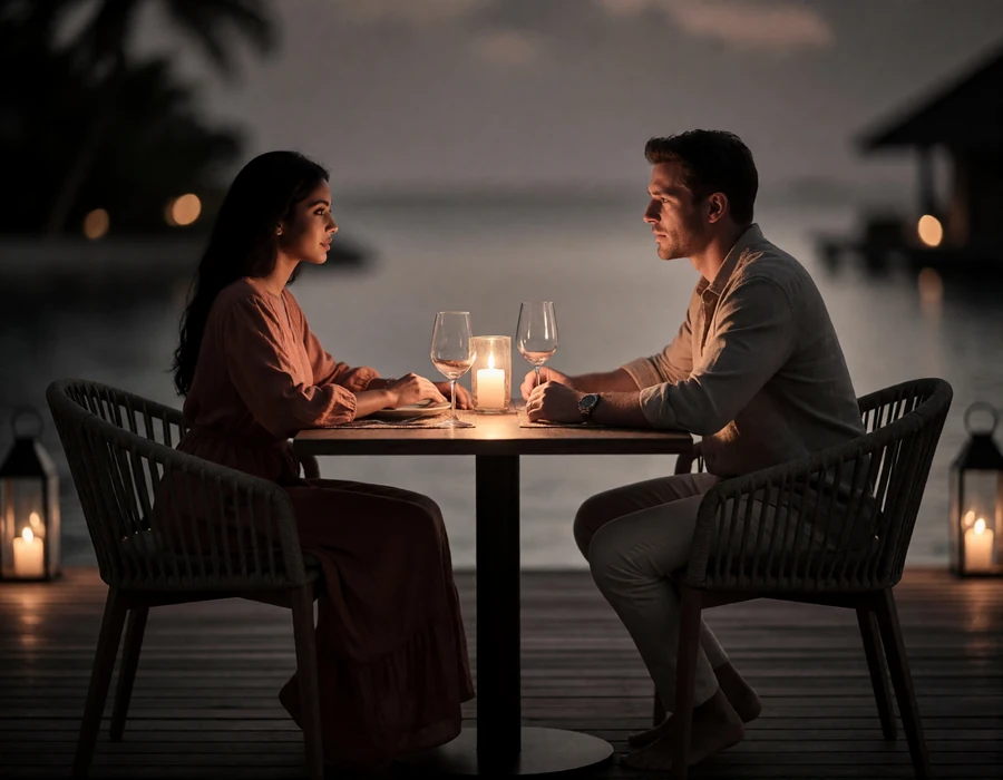 Couple sharing a quiet dinner conversation on an open-air deck at dusk with soft lantern light.